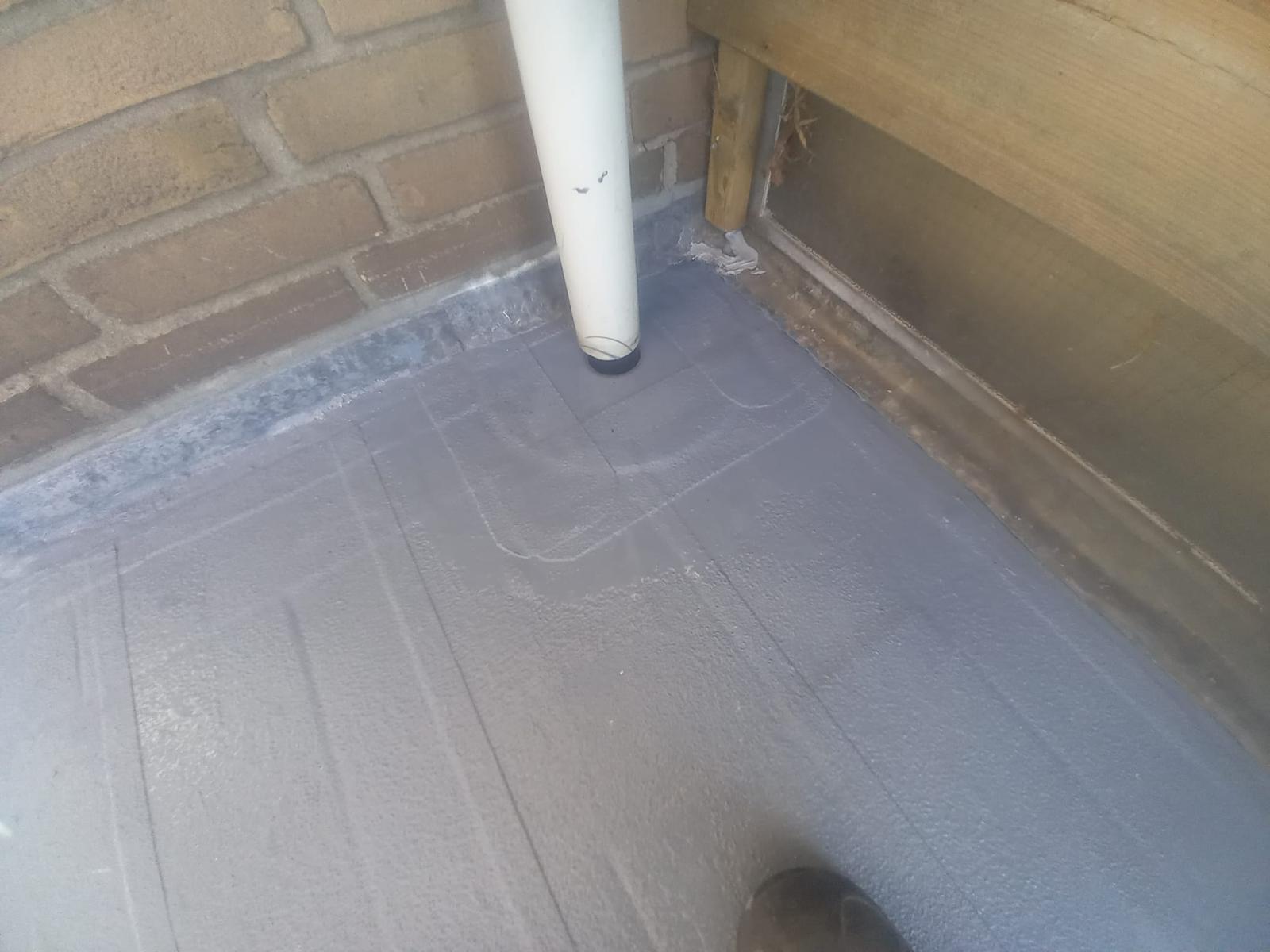 Hoek van een balkon of dak bij bakstenen muur en regenpijp, afgedicht met grijze vloeibare afdichting.
