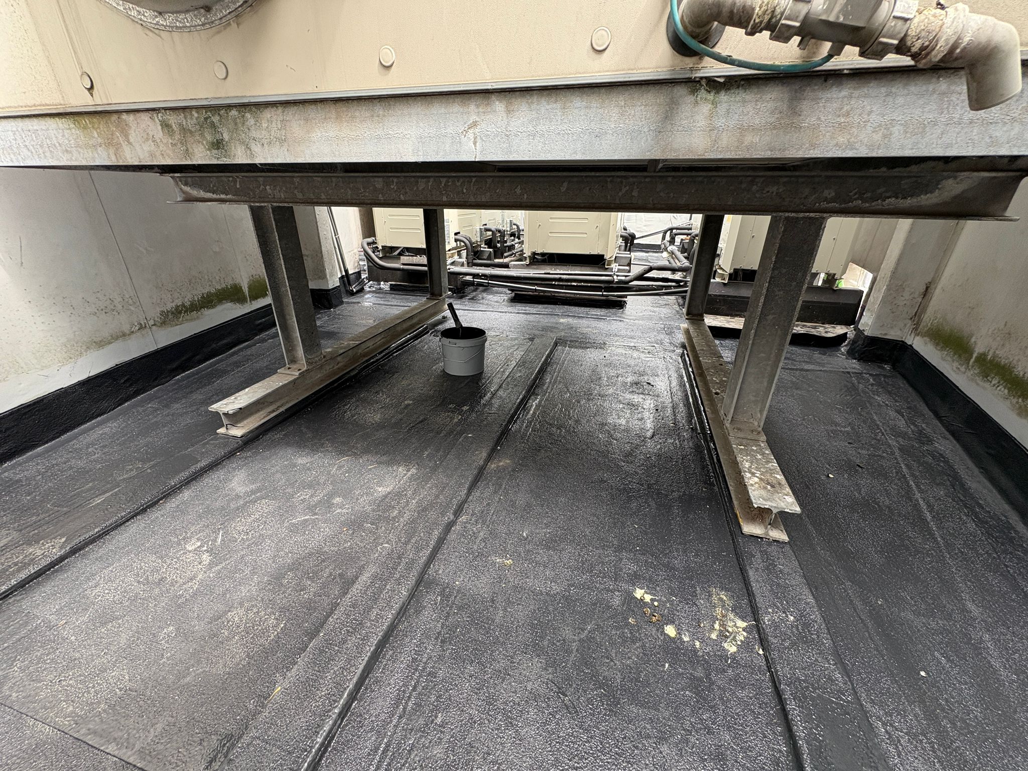 Zwarte gewapende vloeibare afdichting op de dakvloer onder een technische installatie, aangesloten op de stalen poten.